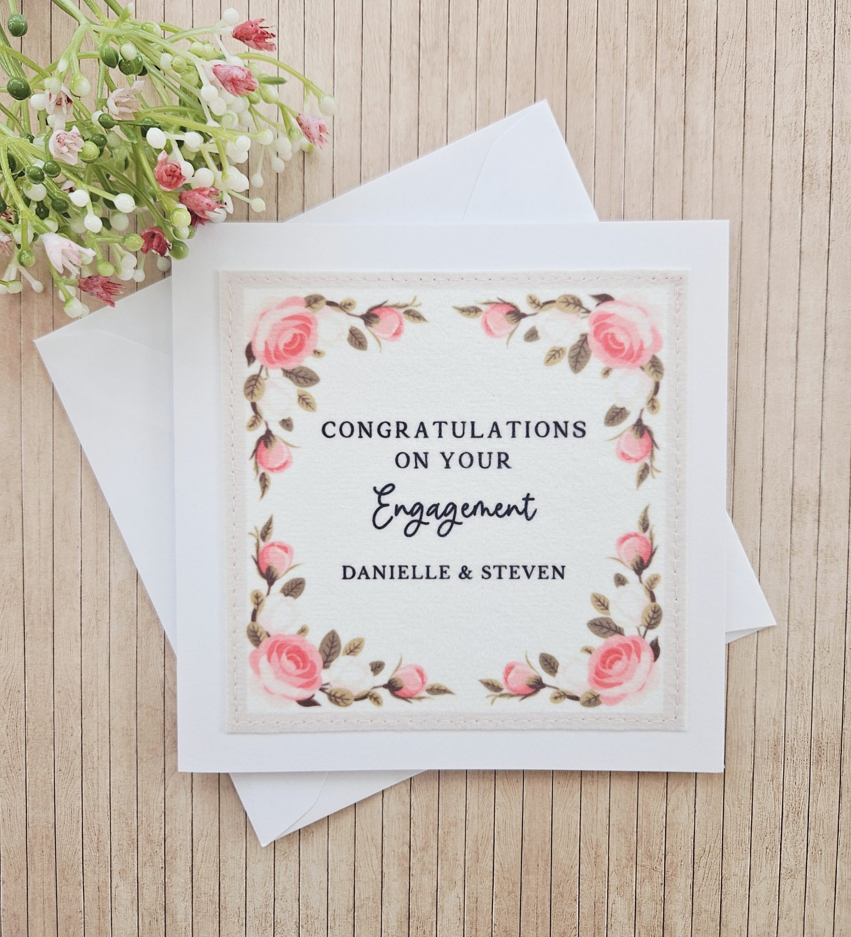 Handmade floral engagement card with white envelope on wooden background