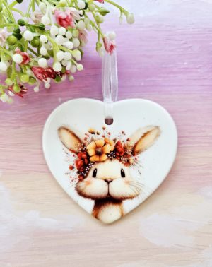 Floral bunny ceramic heart decoration with rabbit wearing a flower crown, hanging on white ribbon against soft pink background.