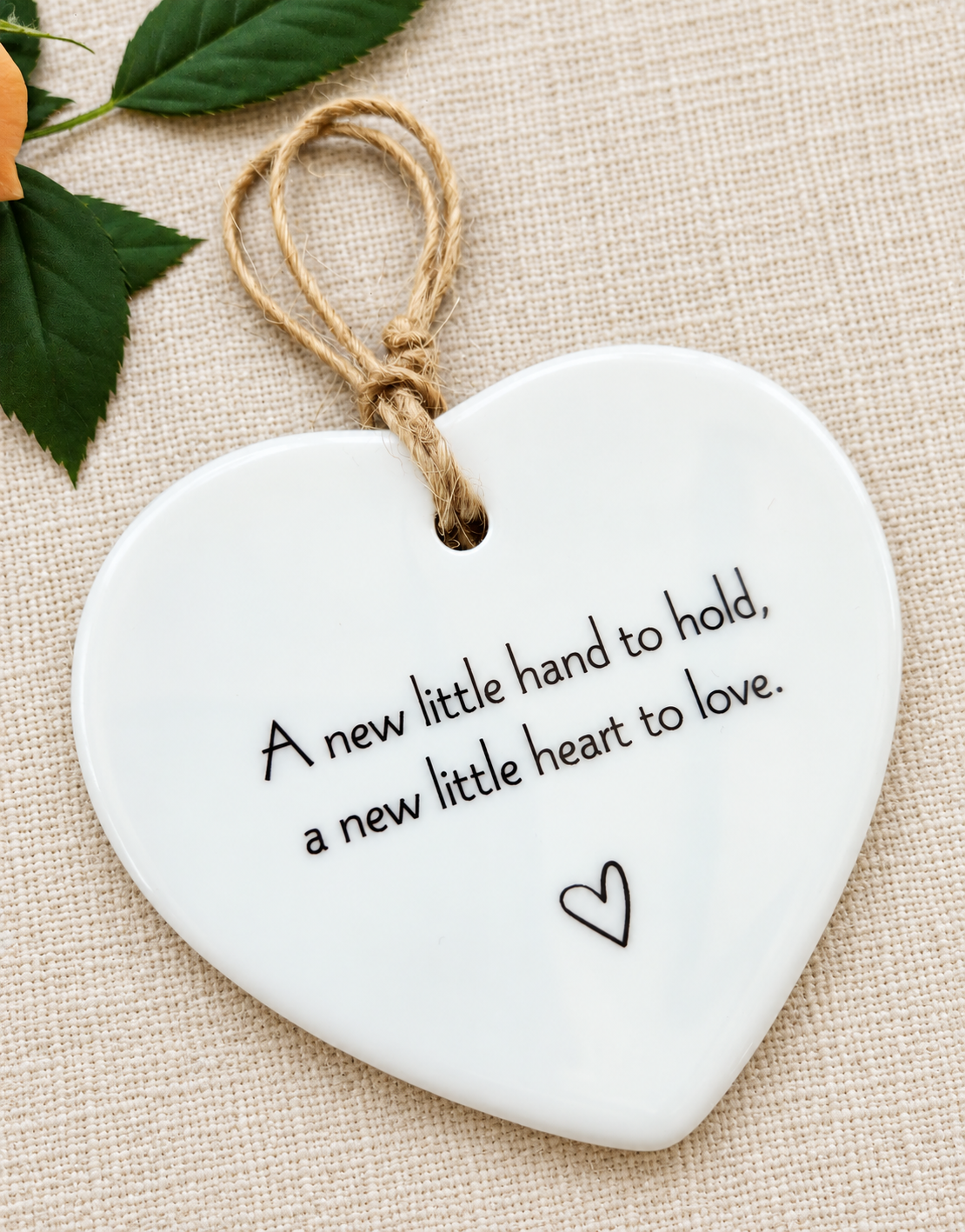 Close-up of handmade new baby ceramic heart decoration with heartfelt quote, natural jute twine and small heart illustration, baby shower gift
