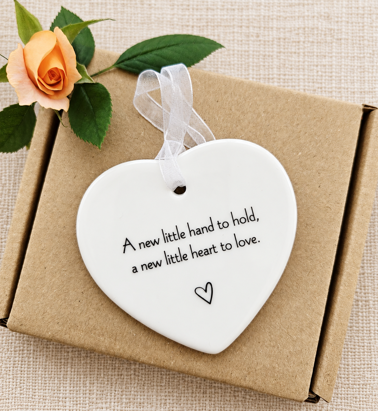 New baby ceramic heart keepsake with white organza hanging ribbon, presented on a kraft gift box with peach rose, thoughtful newborn present