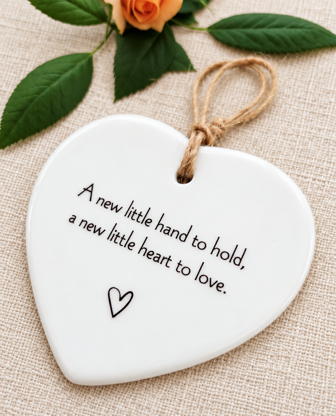 White ceramic hanging heart with sentimental new baby quote, styled with natural twine and peach rose on linen, christening or new baby keepsake gift