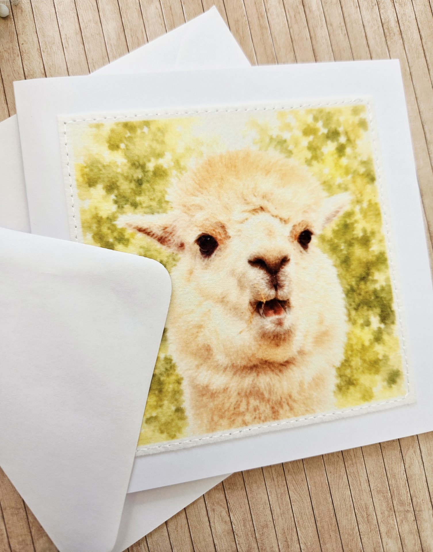 Angled close up view of a handmade fabric print alpaca card showing the texture of the materials and watercolor detail.