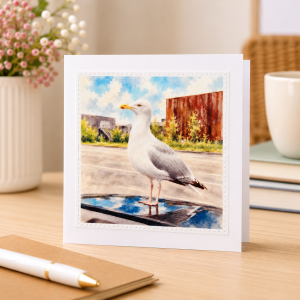 Handmade seagull greeting card standing upright on a wooden desk alongside small seaside decorations.