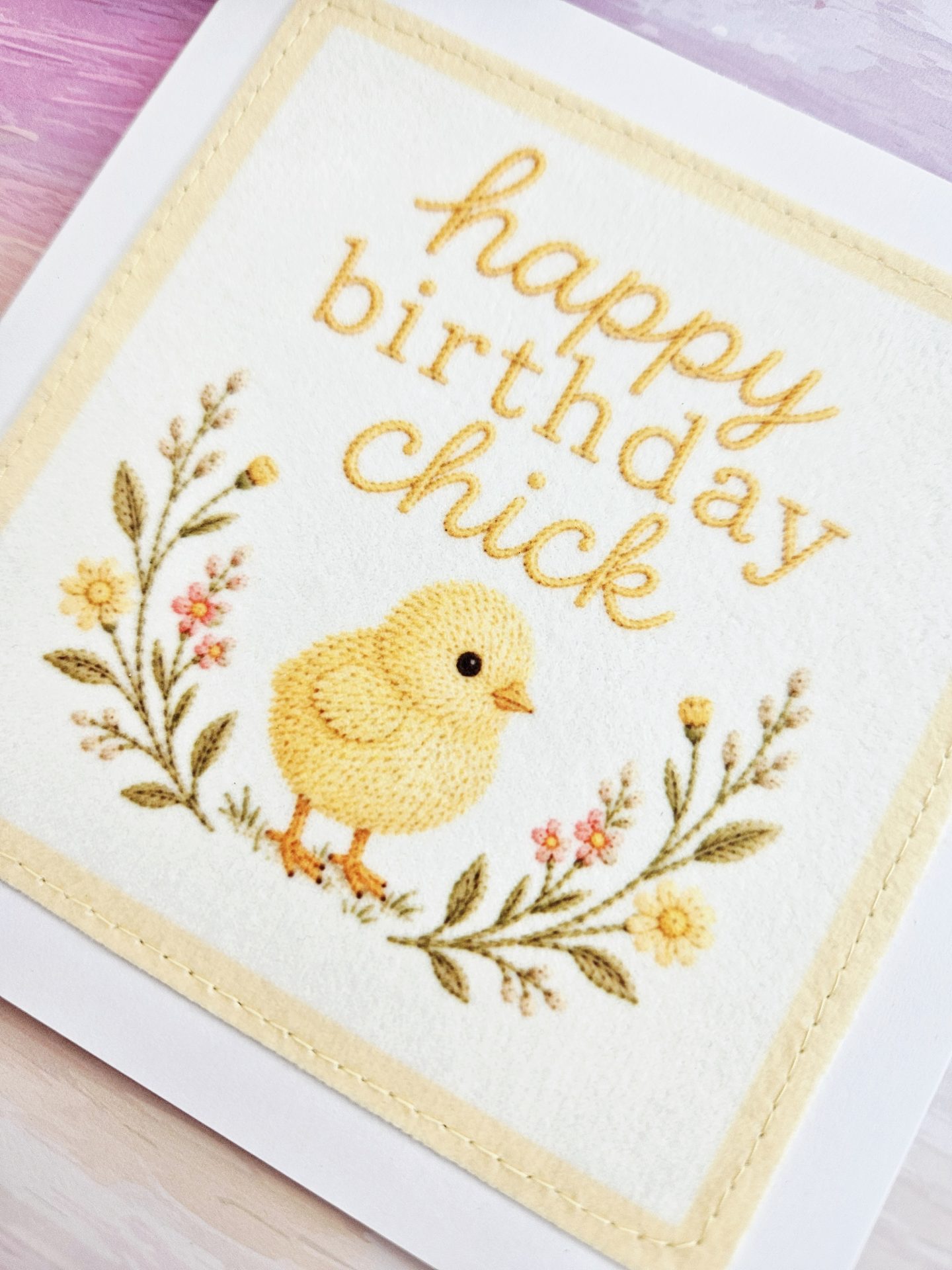 Close-up of the embroidered fluffy yellow chick illustration on the handmade birthday card, surrounded by floral sprigs.