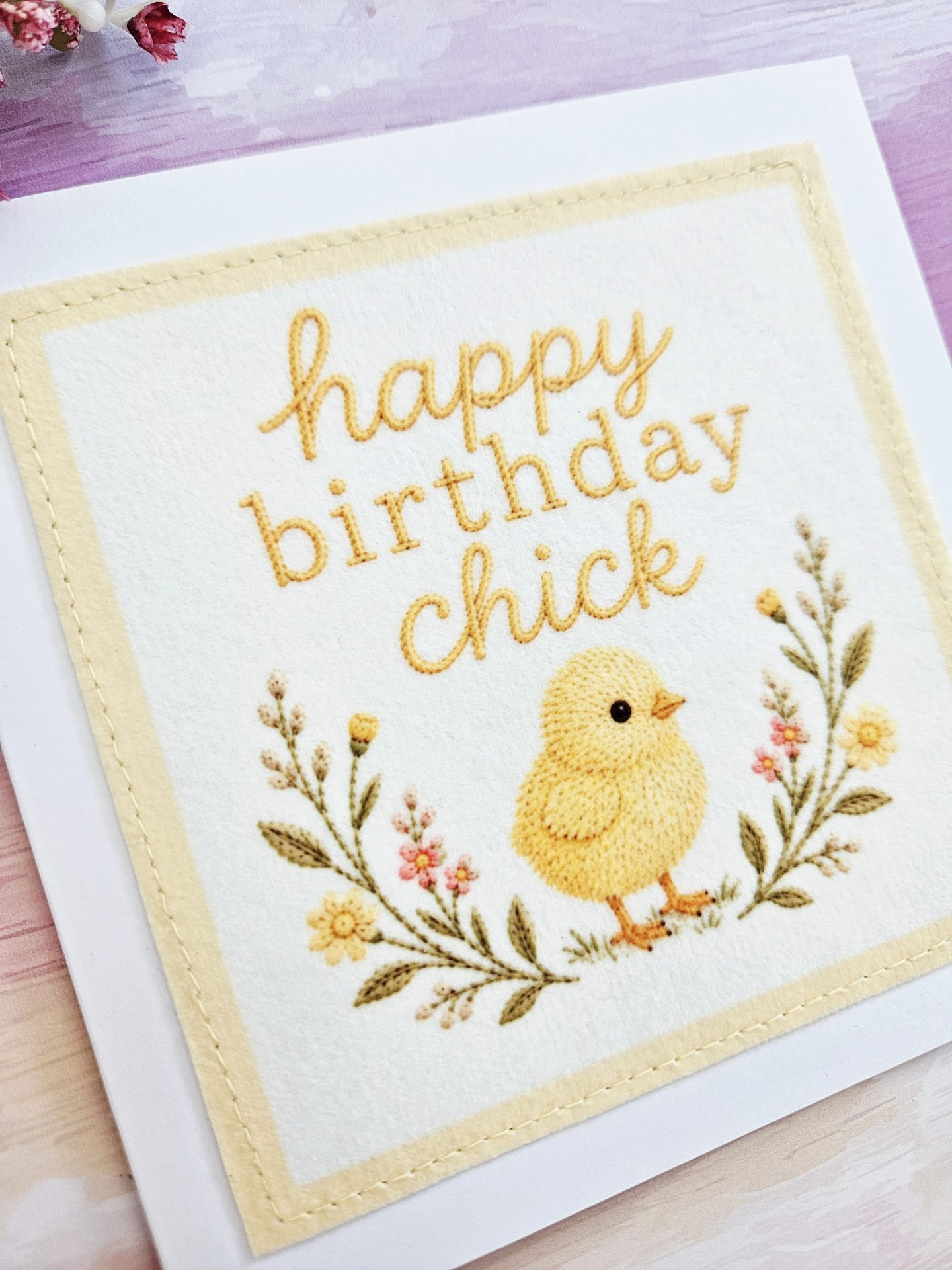 Angled view of the handmade birthday chick card showcasing the textured fabric panel and embroidered design.