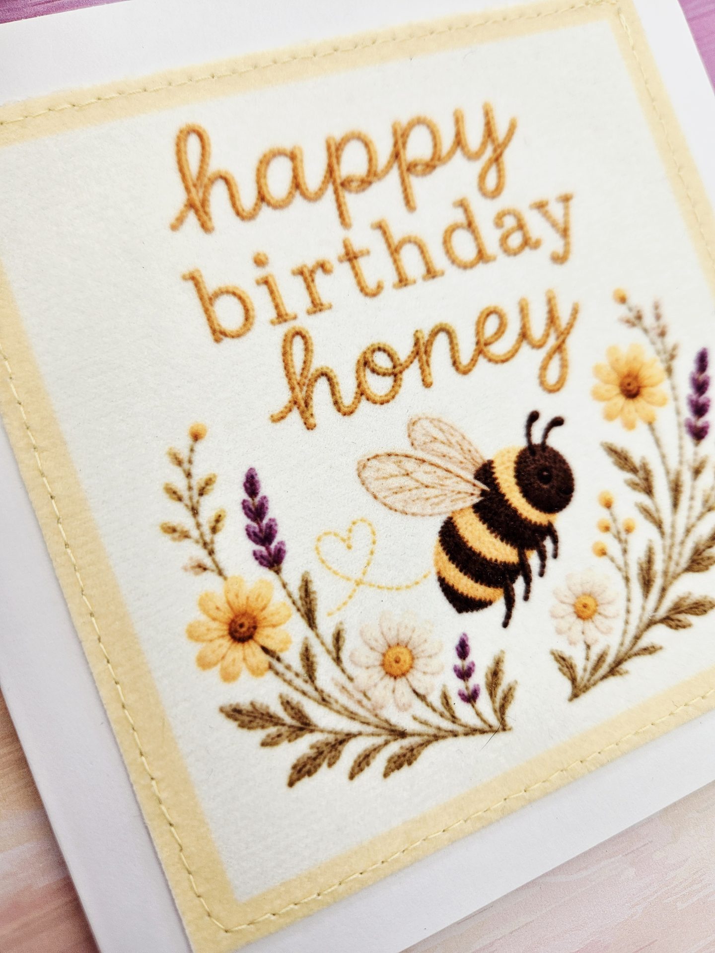 Close up of stitched fabric bee birthday card with wildflowers
