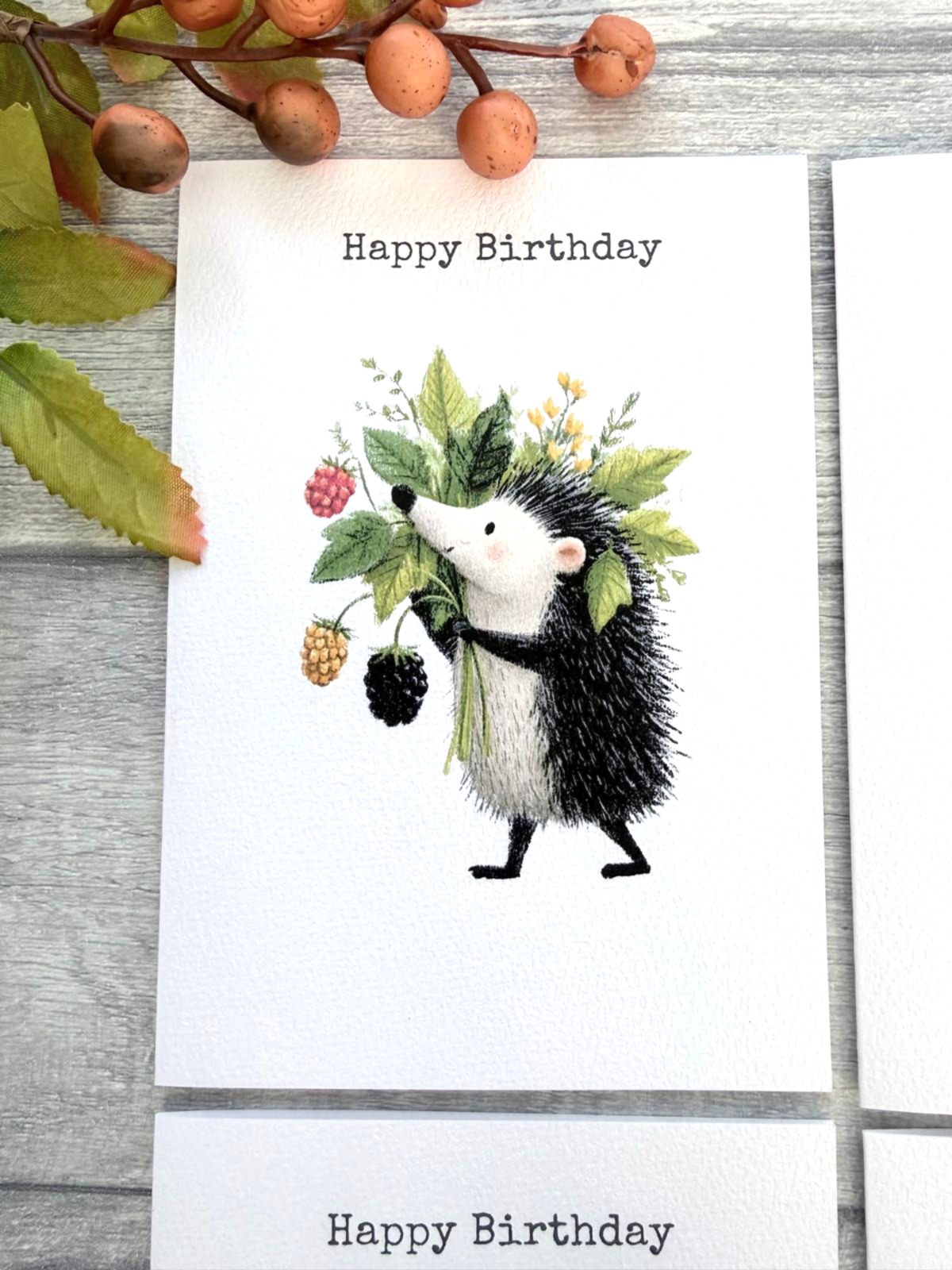 Handmade woodland birthday card with hedgehog carrying berries and leafy foliage