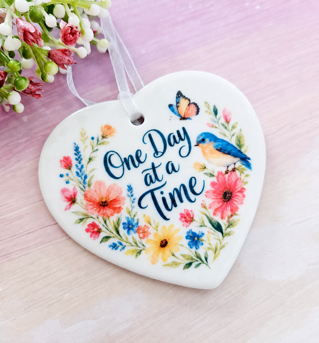 Close-up shot of the One Day at a Time ceramic heart ornament featuring colorful floral details, a blue bird, and a butterfly.
