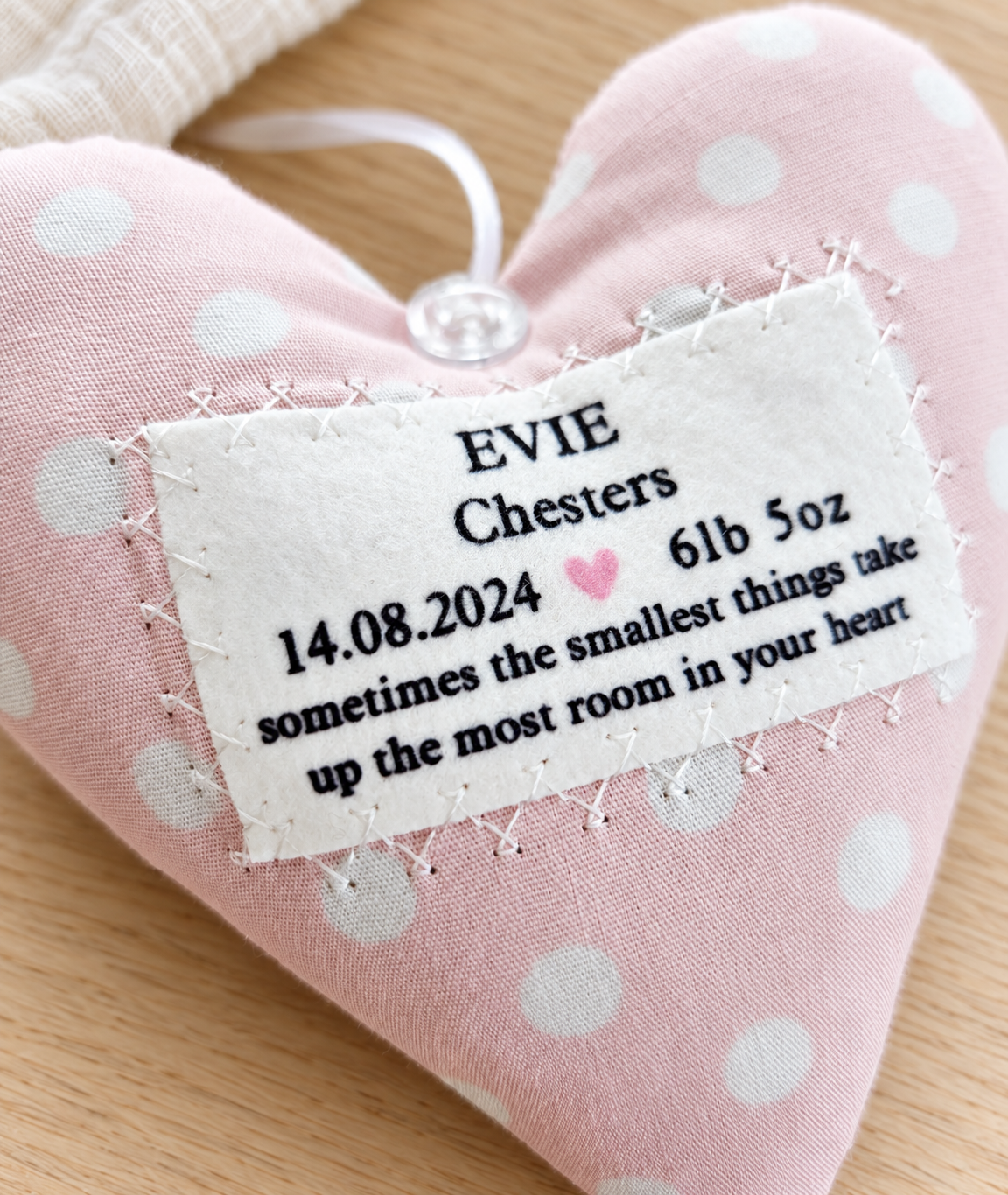Close-up of personalised baby girl fabric heart showing birth date, birth weight, pink heart detail and hand-stitched label, a thoughtful new baby keepsake gift.