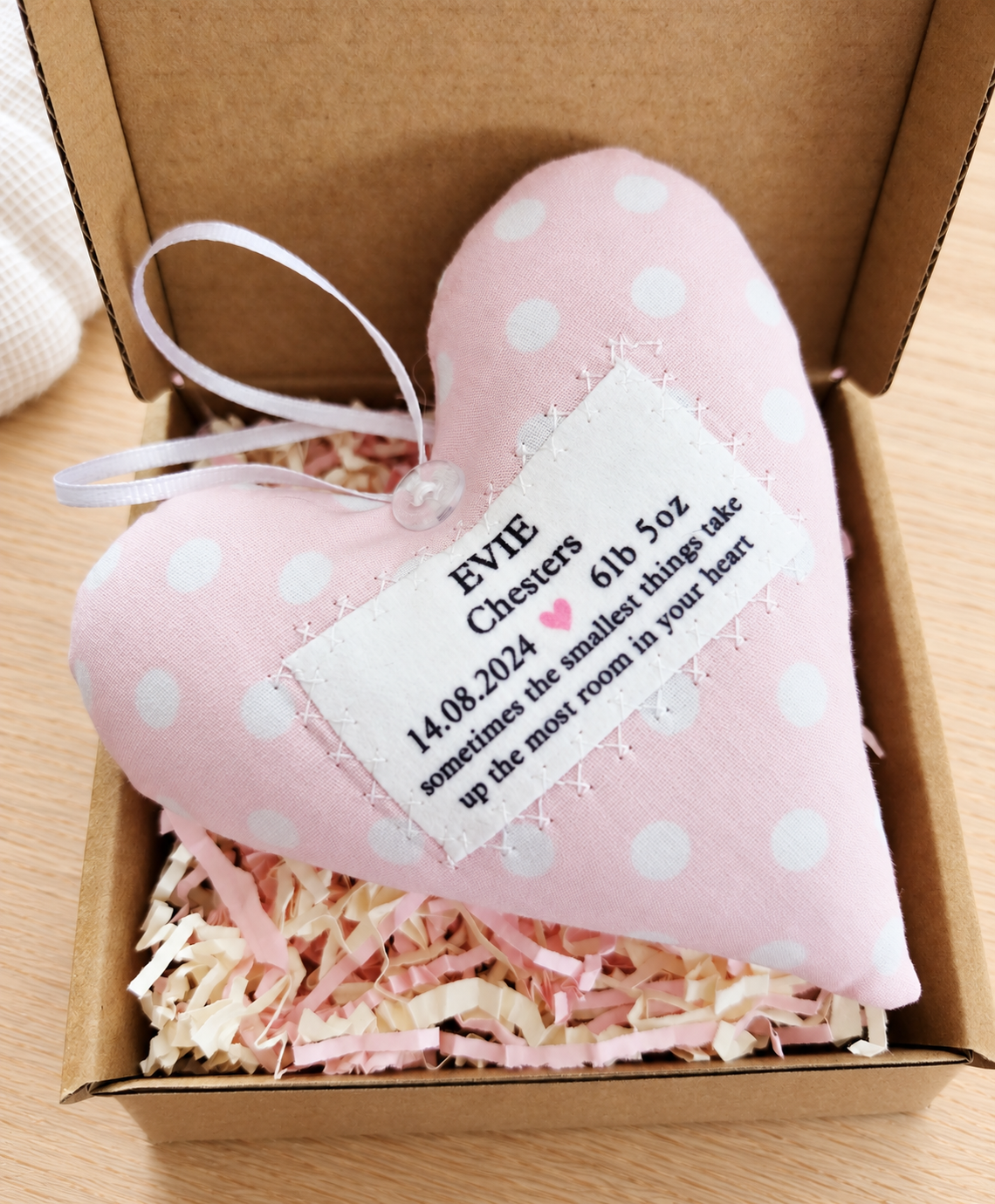 Personalised pink fabric hanging heart for a baby girl, displayed in a gift box with soft pink and cream shredded paper, a thoughtful christening or baptism keepsake.