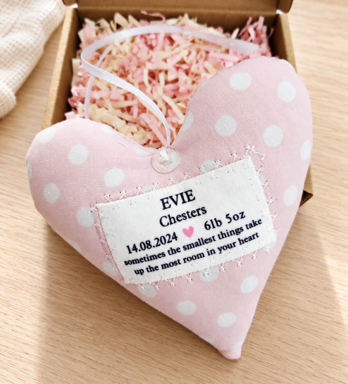 Close-up of handmade pink polka dot baby girl fabric heart with personalised birth details, satin hanging ribbon and gift box, a lovely new baby or naming day gift.