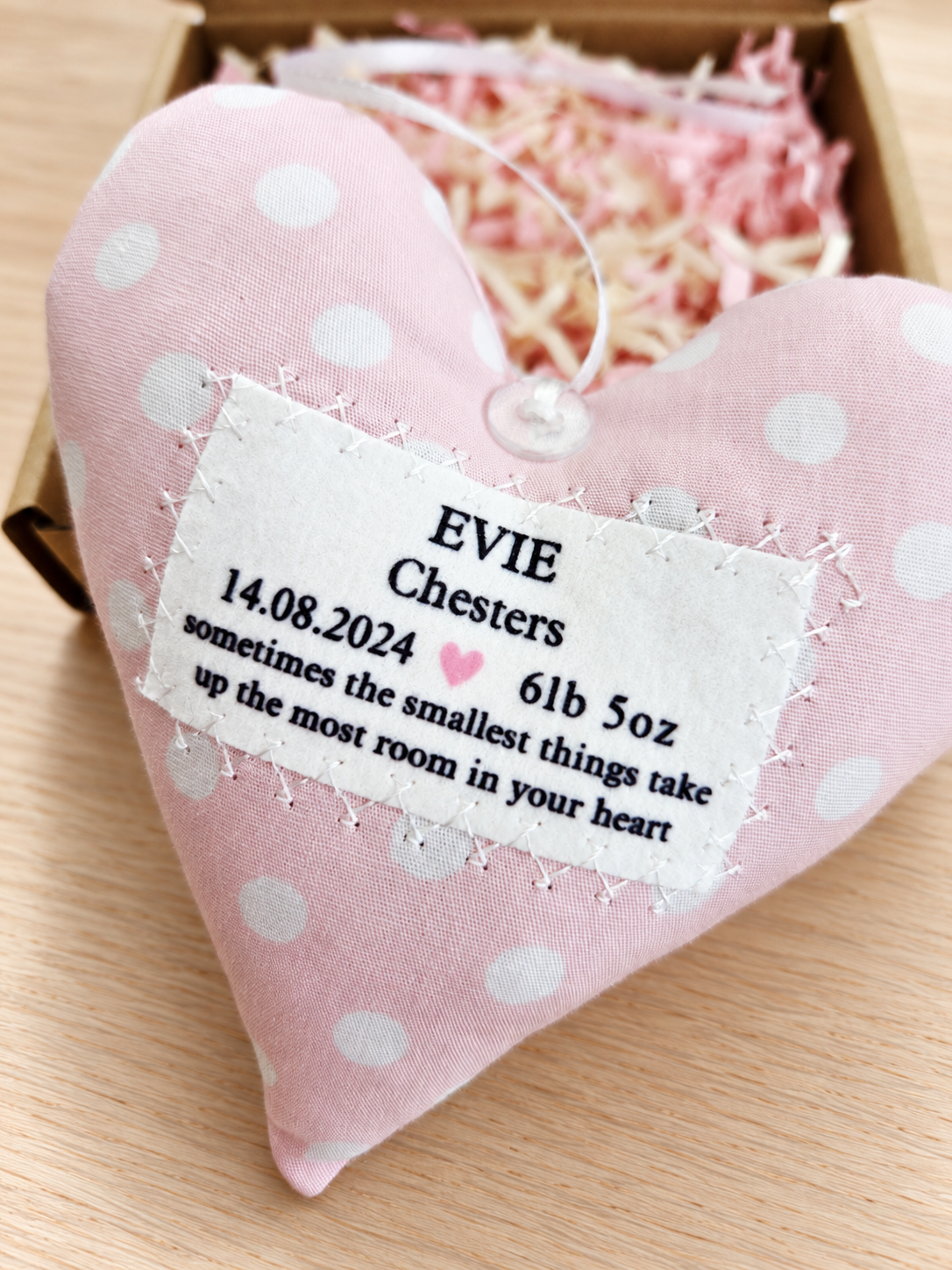 Angled view of personalised baby girl fabric hanging heart in pink and white spotted cotton, with decorative stitching and birth details, a handmade nursery keepsake gift.